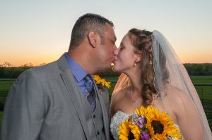 bride and groom kissing while holding sunflowers